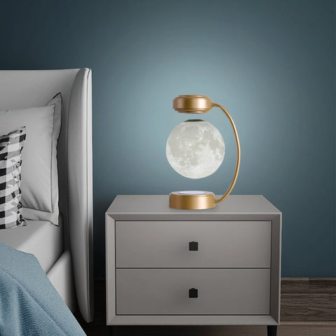 Modern bedside table with levitating moon lamp in golden frame beside grey upholstered bed