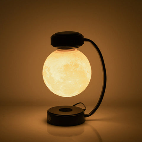 Modern moon lamp floating above black curved stand, warm glowing light in dark room