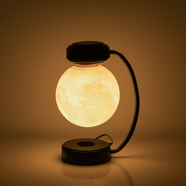 Modern moon lamp floating above black curved stand, warm glowing light in dark room