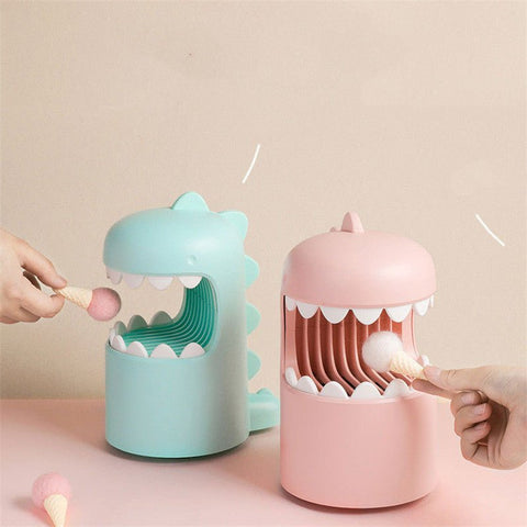 Pink and blue dinosaur-shaped silicone finger guards for holding small objects on a beige background