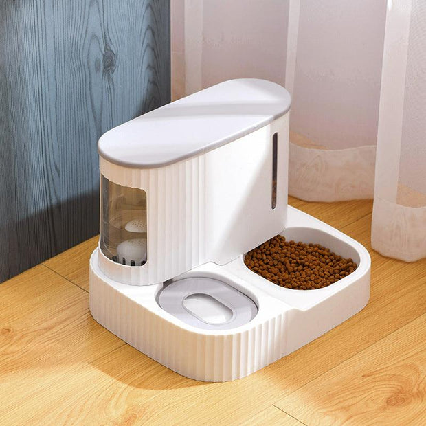 White automatic pet feeder and drinking fountain with separate compartments for food and water on wooden floor