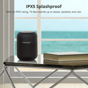 Black Tronsmart T6 Max Bluetooth speaker on a table with a book, by a window showing ocean view