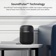 Black Tronsmart portable Bluetooth speaker on a white table next to a blue sofa in a modern room