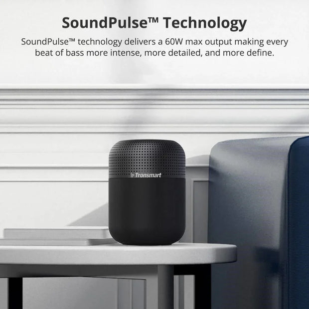 Black Tronsmart portable Bluetooth speaker on a white table next to a blue sofa in a modern room