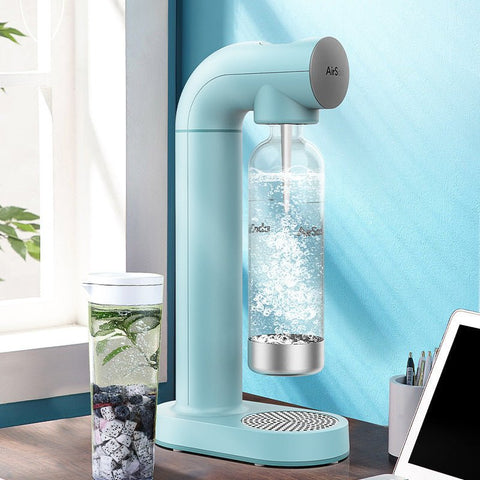 Light blue home soda maker carbonating water in a plastic bottle on a wooden desk near a window