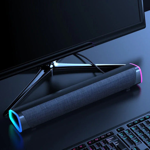 Modern black soundbar speaker with colored LED lights under a computer monitor on a black desk