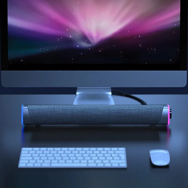 Compact portable speaker with fabric cover and RGB lighting placed in front of a desktop computer on a black desk