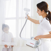 Woman using white Deerma handheld steam cleaner with brush on window curtain next to smiling child