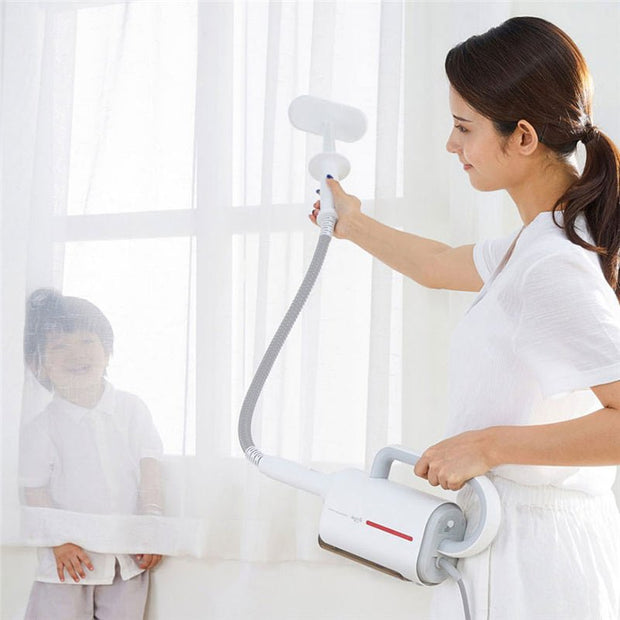 Woman using white Deerma handheld steam cleaner with brush on window curtain next to smiling child