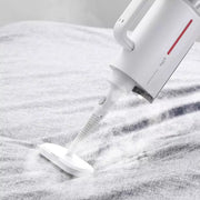 White Deerma ZQ610 steam cleaner in use, emitting steam on a fabric surface, handheld design
