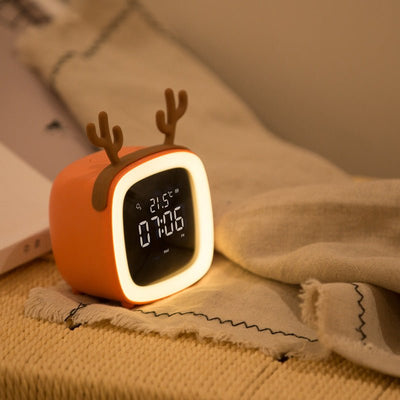 orange digital desk clock with illuminated border and reindeer antlers showing 07:06 and 21.5°C on beige fabric surface