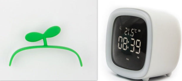 White digital desk clock with thermostat display showing time 08:39 and temperature 21.5°C, with small green sprout decoration