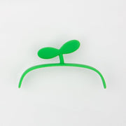 Green silicone hair clip shaped like a small plant sprout on white background