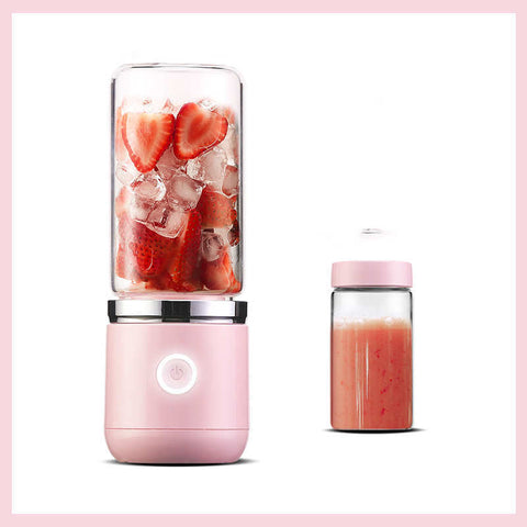 pink portable electric blender filled with strawberries and ice, next to a bottle of blended strawberry smoothie