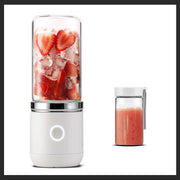 Portable electric juicer with strawberry and ice inside, next to a small container of fresh strawberry juice