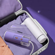 Foldable handheld garment steamer in purple and white inside a gray suitcase on purple fabric