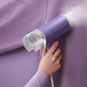 Handheld purple garment steamer removing wrinkles from matching purple fabric