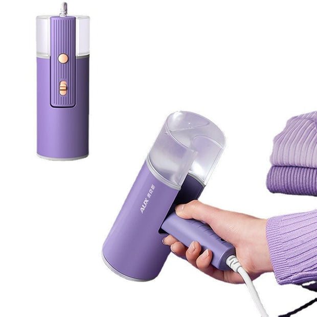 Purple foldable handheld garment steamer with transparent water tank, held by hand, next to folded purple clothes