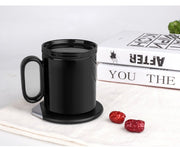 Black ceramic mug on a round induction warming coaster with books and red dates on a white cloth