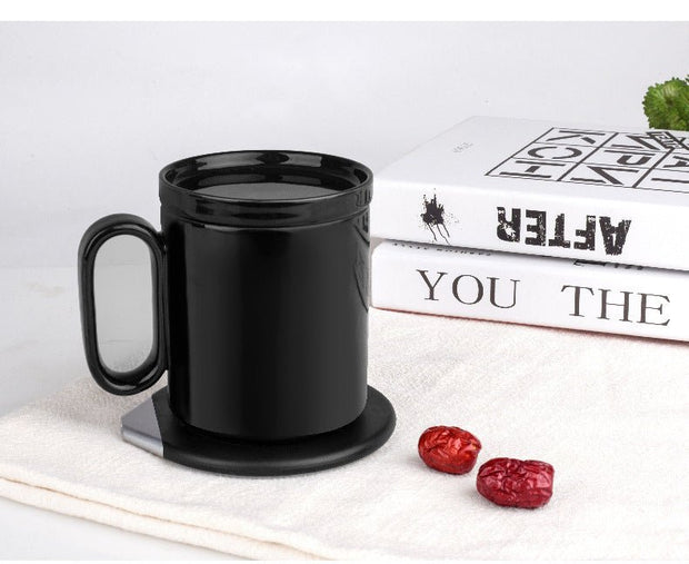 Black ceramic mug on a round induction warming coaster with books and red dates on a white cloth