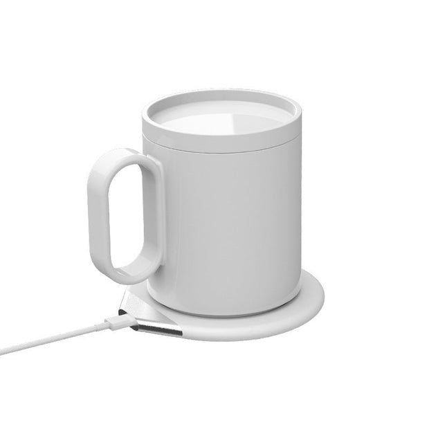 White ceramic mug on a white induction heating coaster with USB cable on a white background