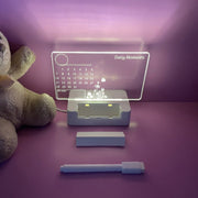 Light-up message board calendar on a purple surface with a marker and eraser, teddy bear beside