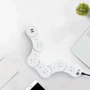 White modular smart power strip with multiple outlets and USB ports on a white desk near laptop and smartphone