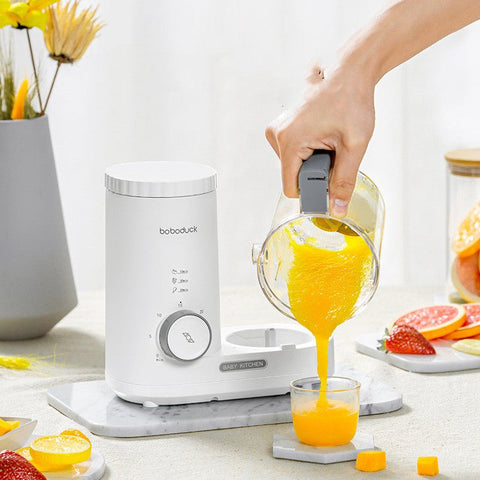 White multifunctional baby food machine pouring fresh orange puree into a glass on countertop