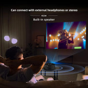 Man watching concert video projected on wall with portable mini projector featuring built-in speaker