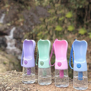 Portable pet water bottles in purple, green, pink, and blue with attached drinking bowls outdoors