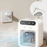 White mini air cooler plugged into wall outlet blowing cool air on wooden surface
