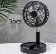 Black portable telescopic folding fan on white surface with green plant in background