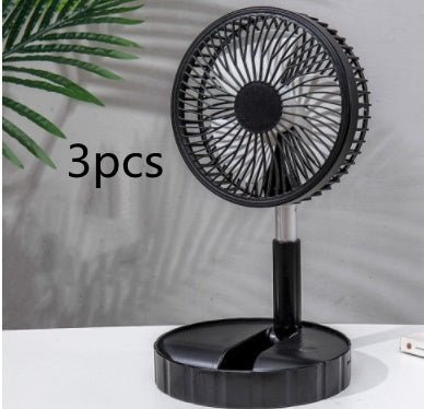Black portable telescopic folding fan on white surface with green plant in background