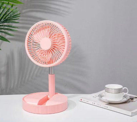 Pink portable telescopic folding fan on white table with a teacup and magazine, gray background