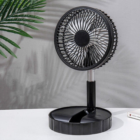 Black portable telescopic folding desk fan on white surface with plant shadow in background