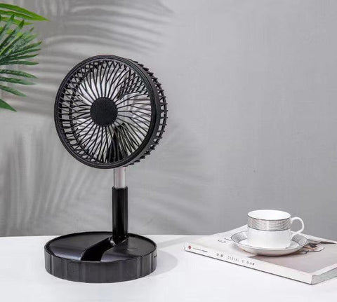 black portable telescopic folding fan on white table next to book and cup with plant shadow on gray wall