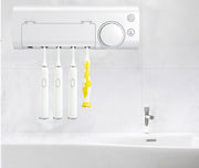 Wall-mounted white UV toothbrush sterilizer holding four electric toothbrushes, one with yellow accents, above a white sink with chrome faucet