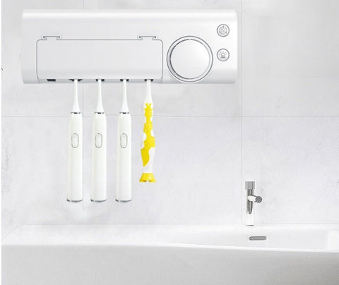 Wall-mounted white UV toothbrush sterilizer holding four electric toothbrushes, one with yellow accents, above a white sink with chrome faucet