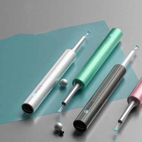 Four wireless ear cleaners in silver, green, black, and pink with silicone tips on gray and blue background