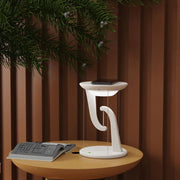 Modern white wireless floating charger on round table with smartphone, book, and plant backdrop