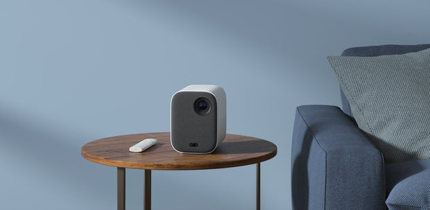 Xiaomi smart projector on wooden side table next to blue sofa and cushion in minimalist room