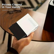 Hand holding compact white and black mini projector on wooden table with 'Private Cinema in Your Hands' text