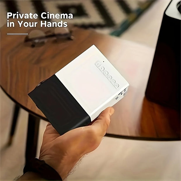 Hand holding compact white and black mini projector on wooden table with 'Private Cinema in Your Hands' text
